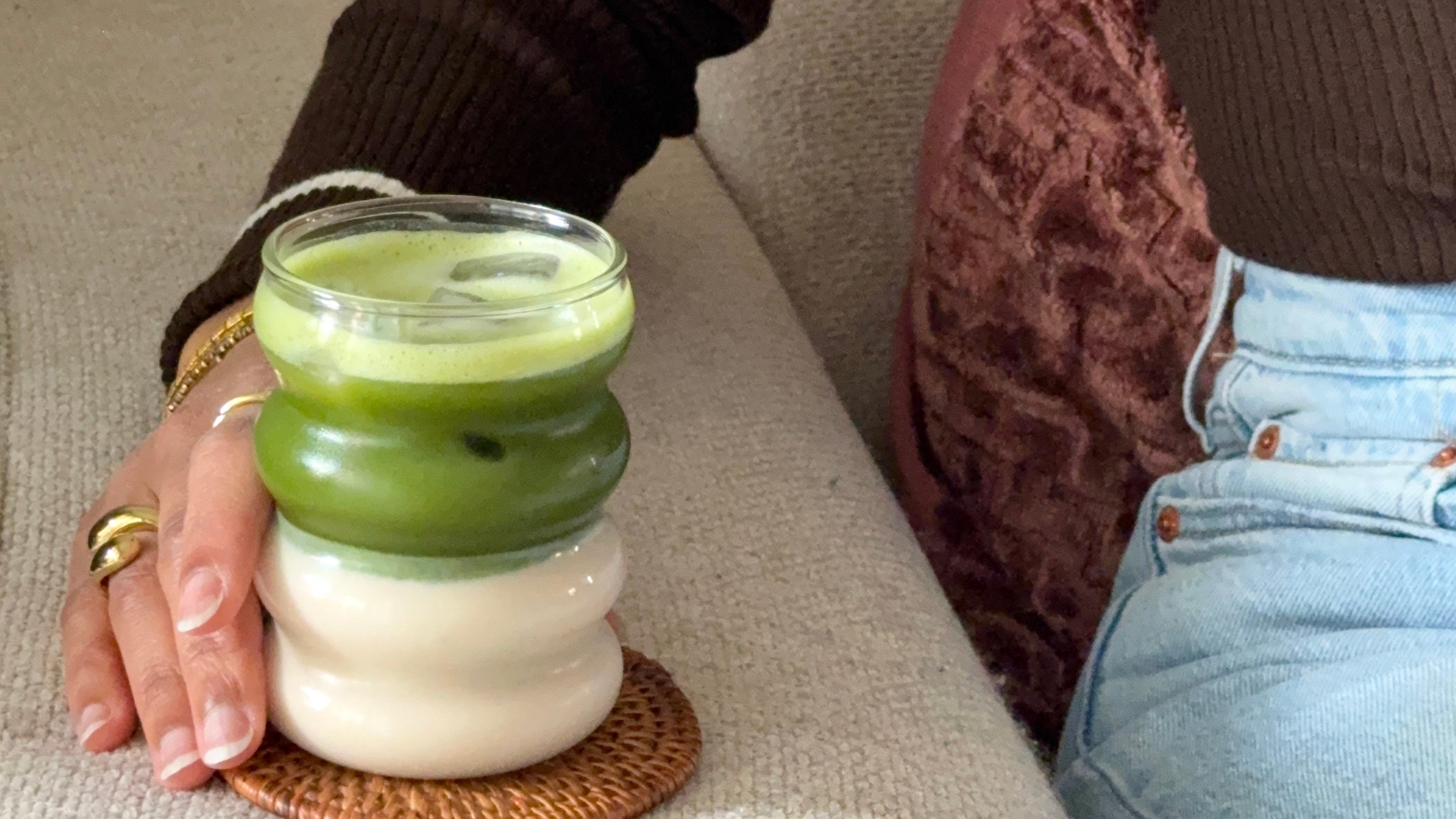 Femme tenant un ice matcha latte sur l'accoudoir d'un canapé en tissu.